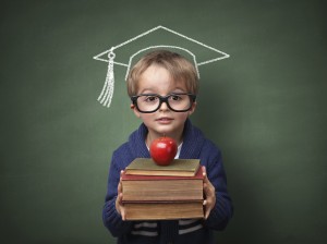 Child holding stack of books with mortar board chalk drawing on blackboard concept for university education and future aspirations