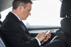 Sending an urgent message. Side view of confident mature businessman typing message on his smart phone while sitting on the back seat of a car